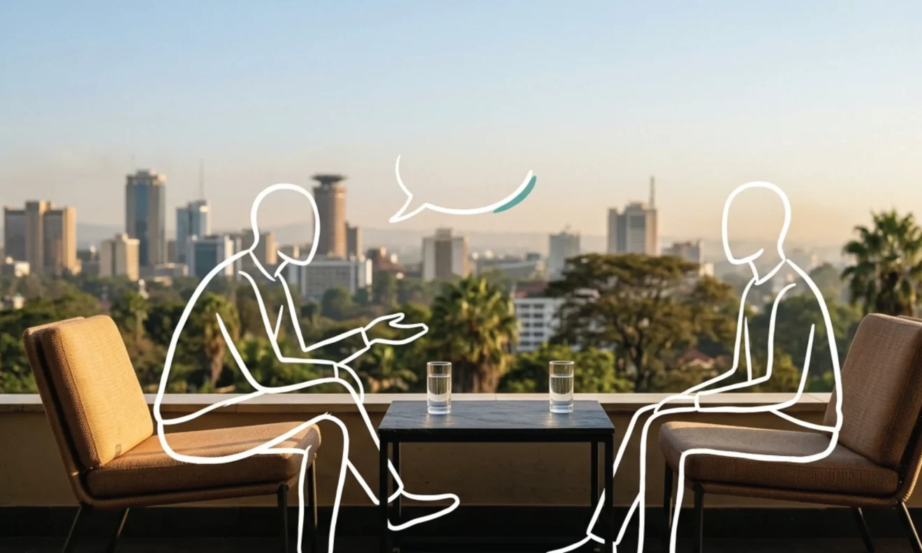 Two empty chairs facing each other on a Nairobi rooftop terrace, the city skyline soft behind, a low slate table between them