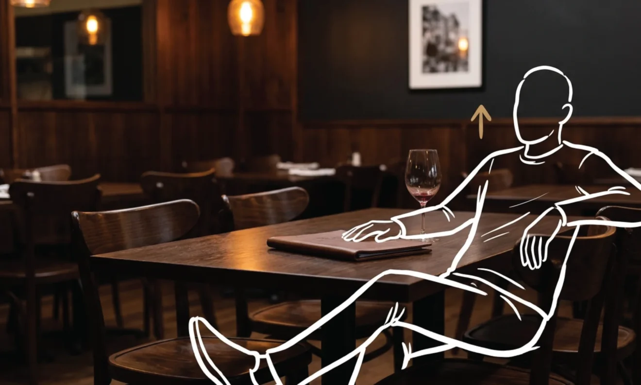 A closed leather receipt folder on a dark timber restaurant table in Nairobi, a near-empty wine glass beside it, warm amber interior light surrounding it